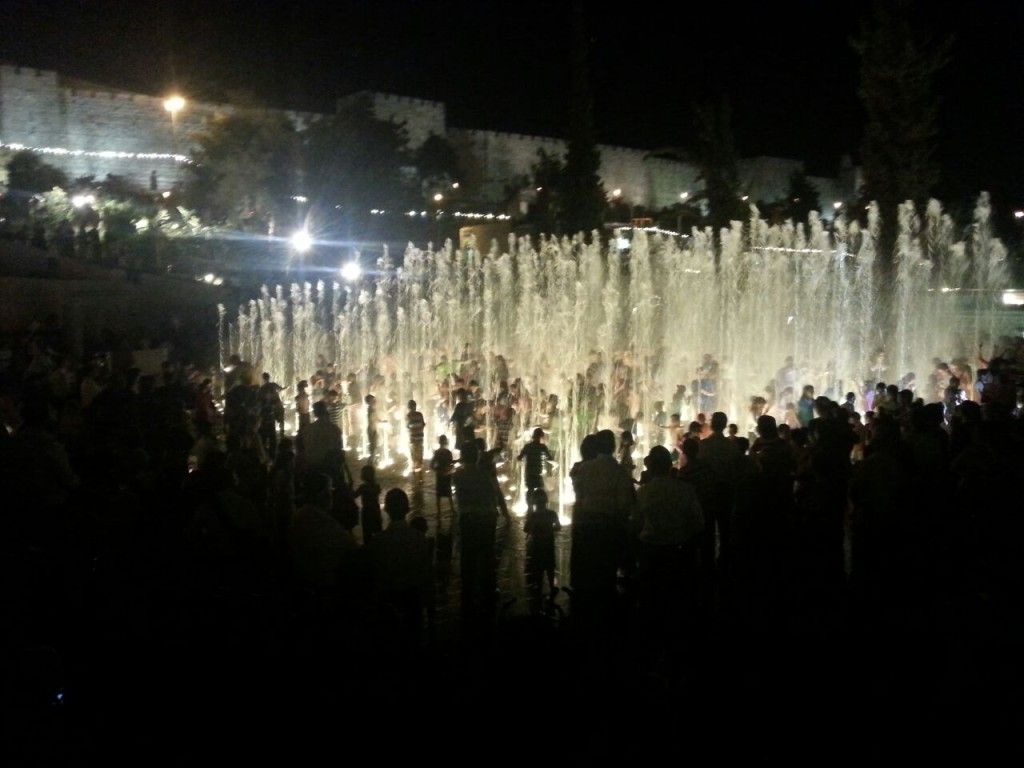 המזרקה בפארק טדי בלילה עם אורות וילדים משתוללים בתוכה